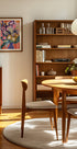 ein gemütliches und gut organisiertes Wohnzimmer mit einem Bücherregal aus Holz, einem runden Holztisch und einem Holzstuhl. Der Raum hat eine warme und einladende Atmosphäre, mit einem Gemälde an der Wand und einer Obstschale auf dem Tisch.
